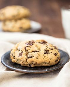 two chocolate chip cookies on a black plate with a glass of milk in the background