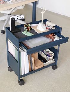 a blue cart filled with lots of books and office supplies on top of a white floor