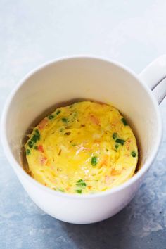 a white cup filled with food sitting on top of a blue countertop next to a spoon