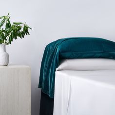 a white vase sitting on top of a bed next to a green blanket and pillow