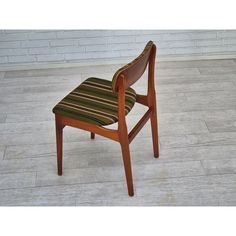 a wooden chair with striped seat padding on the floor in front of a brick wall