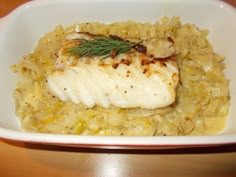 a white plate topped with fish and rice covered in gravy, garnished with a sprig of green