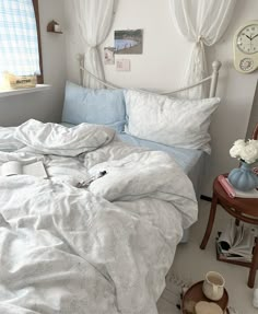 an unmade bed in a bedroom with white curtains and blue comforter on it