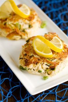 two crab cakes on a white plate with lemon wedges