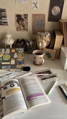 an open book sitting on top of a white table next to a cup and pencils