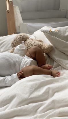 a baby laying on top of a bed next to a teddy bear