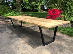 a wooden table sitting in the middle of a park with red flowers behind it,