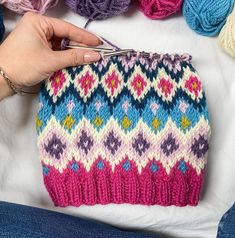 a hand holding a knitting needle next to a knitted bag