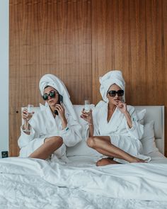 two women sitting on a bed holding wine glasses