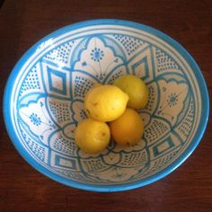 three lemons in a blue and white bowl on a wooden table with an intricate design