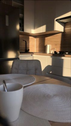 a white cup sitting on top of a wooden table next to a bowl and spoon