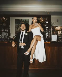 a man standing next to a woman in a white dress at a bar with drinks