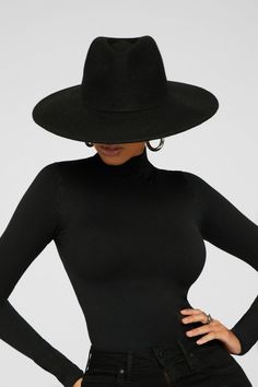 a woman wearing a black hat with her hands on her hips