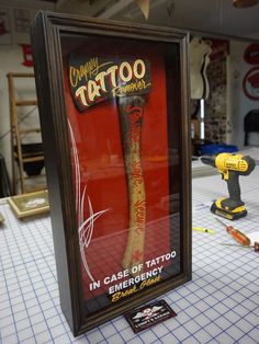 a tattoo sign in a frame on top of a table next to a drill and screwdriver