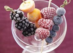 a glass filled with fruit on top of a purple table next to a pink wall