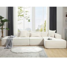 a living room with a large white sectional couch and rug on the floor in front of a window