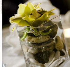 a vase filled with rocks and flowers on top of a white table cloth next to a candle