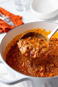 a ladle full of chili and mashed potatoes is being lifted from the pot