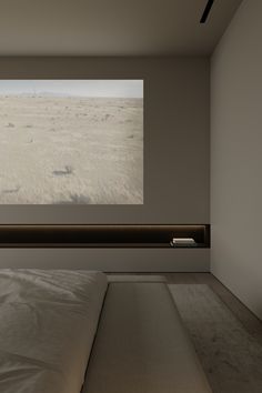 an empty room with a large screen on the wall and a bed in front of it