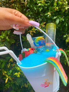 a person holding a toothbrush in a bucket filled with blue liquid and rainbow colors