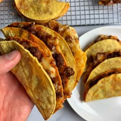 a hand holding up a tortilla with meat and cheese on it next to other food items