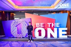 a man standing in front of a large sign with the words be the one on it