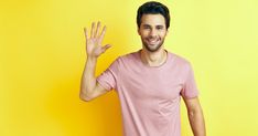 a man in a pink shirt is holding his hand up to the side and smiling