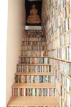 there is a stair case full of books in the room that has a buddha statue on it