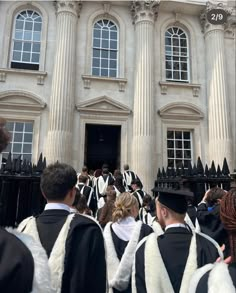 several people in graduation gowns are standing outside the building with their backs to the camera