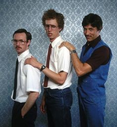 three men standing next to each other in front of a wall