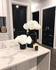 two black vases with white flowers sit on a marble countertop in the kitchen