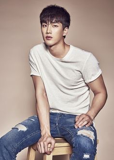 a young man sitting on top of a wooden stool wearing ripped jeans and a white t - shirt