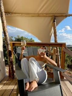 a woman sitting in a chair on top of a wooden deck holding a glass of wine