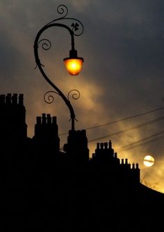 a street light on top of a building with the sun setting in the sky behind it