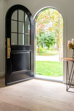 an open door leading to a lush green yard with flowers in vases on the table