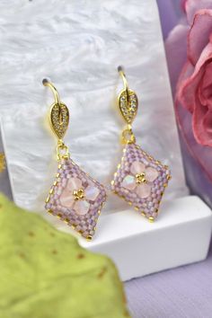 a pair of earrings sitting on top of a white box next to a pink flower