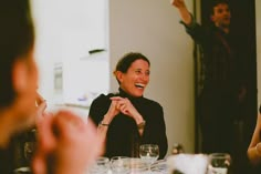 a group of people sitting around a table with wine glasses on the table and one person standing up