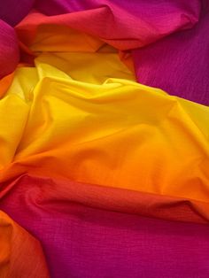 an orange and yellow blanket on top of a purple bed sheet with pink sheets in the background