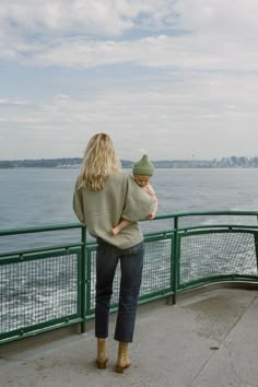 a woman holding a baby while standing on top of a pier