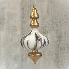 a white and gold hanging ornament on a gray wall with a yellow cord