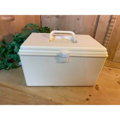 a large white box sitting on top of a wooden floor next to a green plant