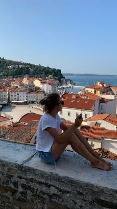 a woman sitting on top of a stone wall next to the ocean