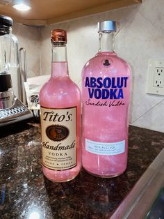 two bottles of absolut vodka sitting on top of a kitchen counter next to a blender