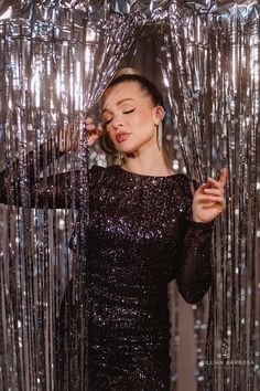 a woman in a black sequin dress is holding her hair up