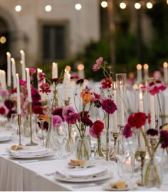 the table is set with candles, plates and vases filled with pink and red flowers