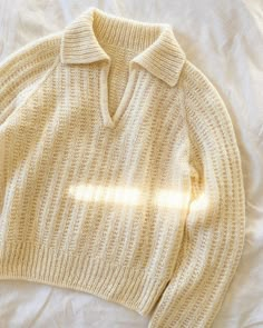 a white sweater laying on top of a bed next to a light shining through the window