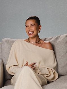 a woman sitting on top of a gray couch next to a white wall and smiling