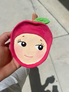 a person holding up a paper cut out of an apple with a face on it