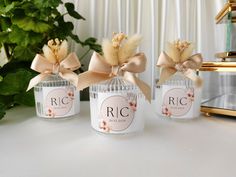 three small jars with bows on them sitting next to a potted plant and mirror