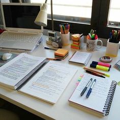 an office desk with notebooks, pens and laptop computer